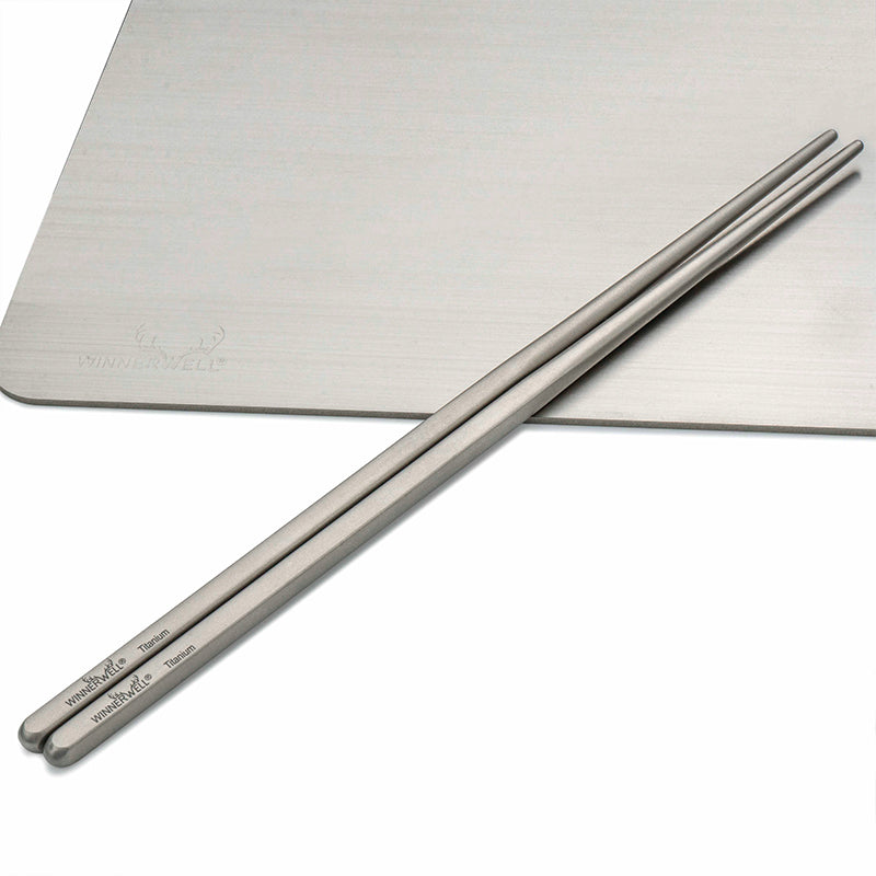 Two Winnerwell® square titanium chopsticks placed side by side on a flat surface, emphasizing their uniform square shape and metallic finish.