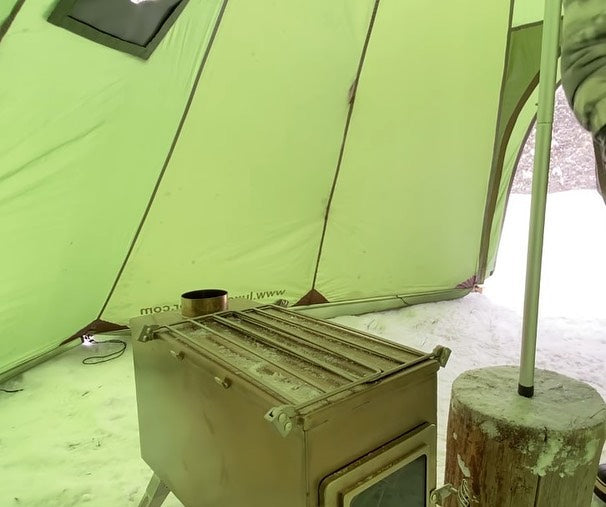 Foldable side shelves on camping stove used as workspace and carry handles for transport