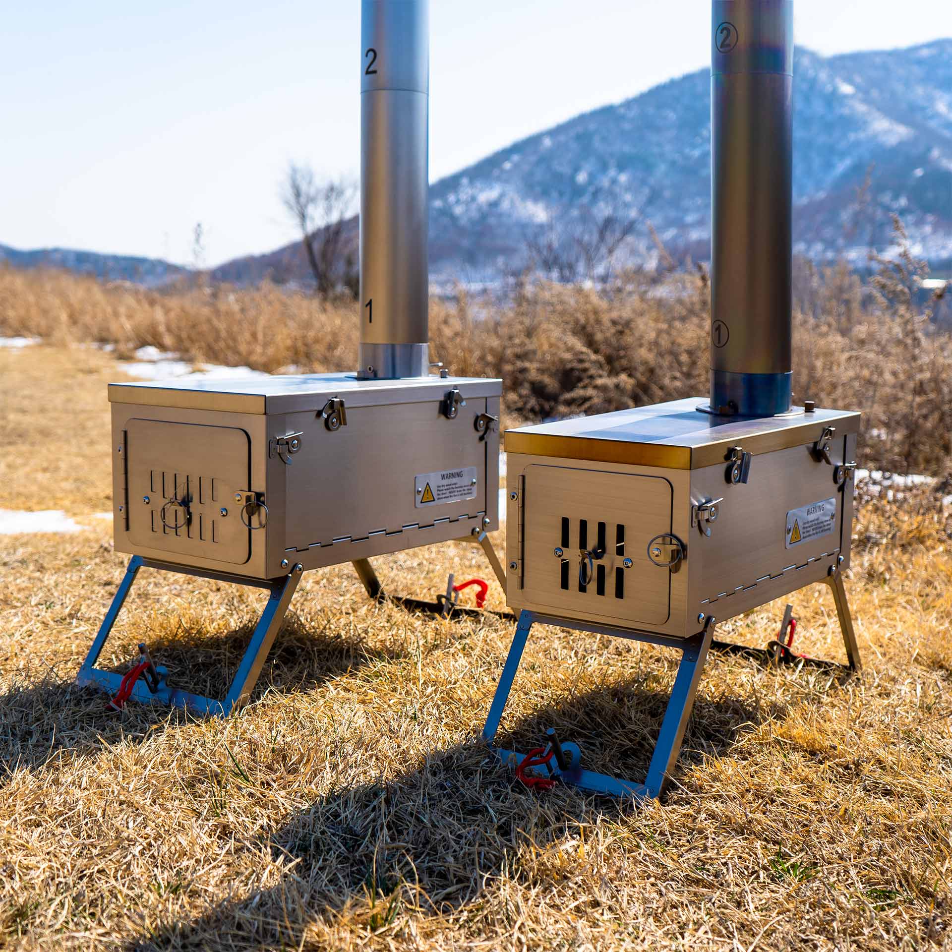Winnerwell® Fastfold Titanium Camping Stove Series. Shows two stoves arranged for camping use, made of lightweight titanium, perfect for group outdoor activities, providing efficient cooking and heating solutions in the wild.